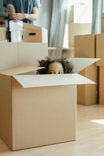 girl peaking out of a moving box as her family goes through relocation