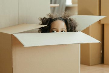 girl peaking out of a moving box as her family goes through relocation